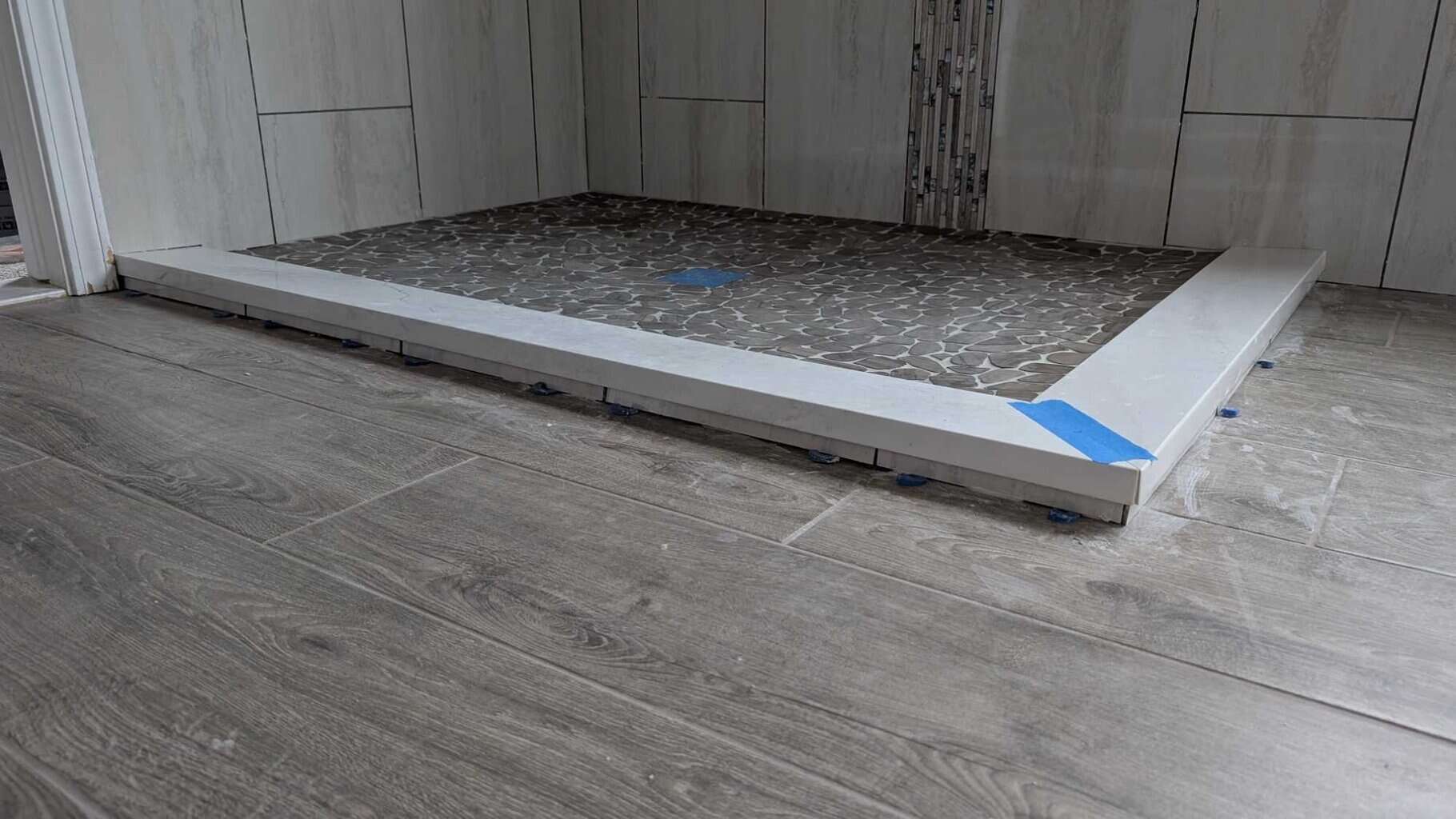 Tiles set under primary shower curb